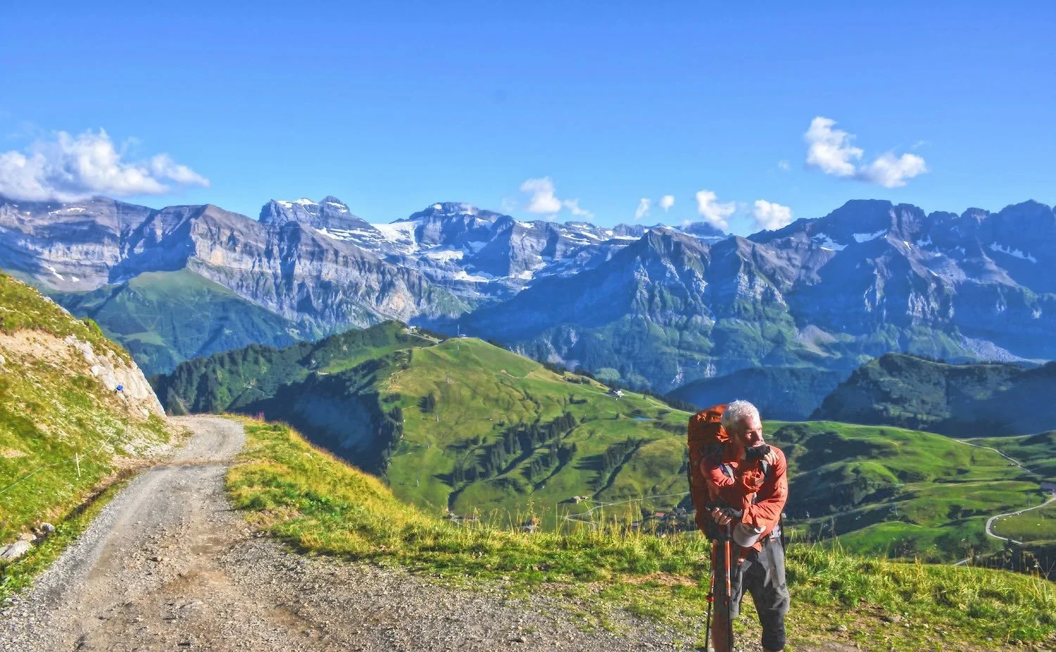 A hiker resting on a green alpine ridge with mountain peaks behind