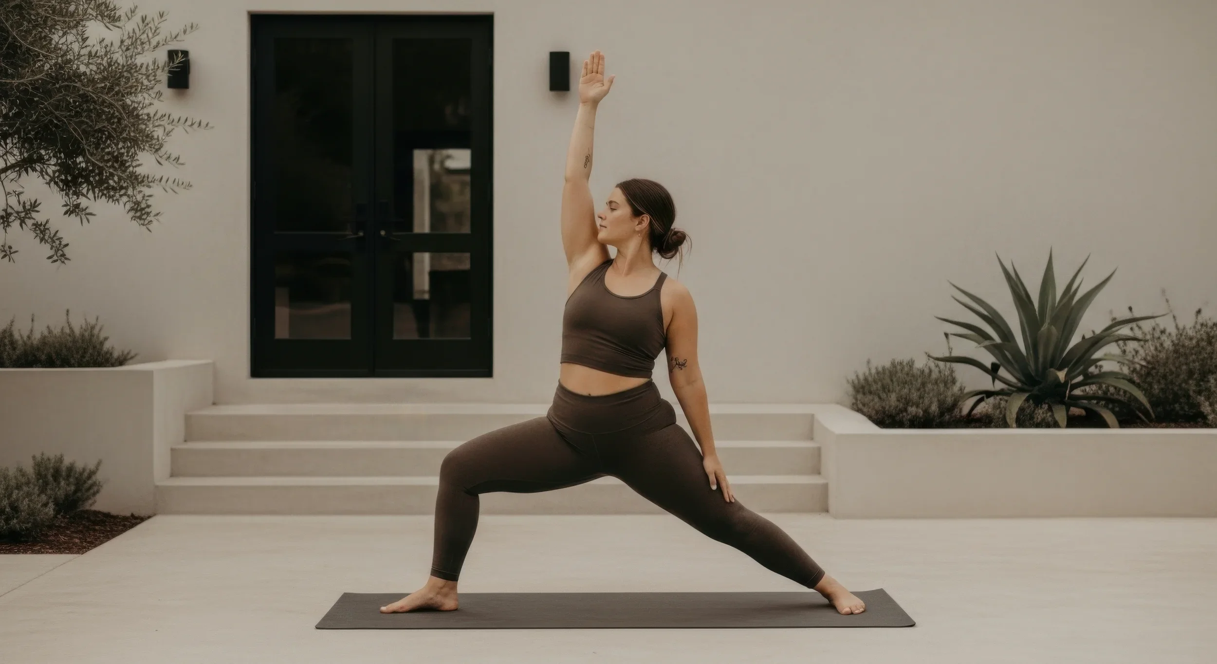 A woman practicing yoga outdoors on a patio, in Warrior Pose with her eyes closed